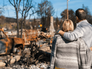 A couple stand looking at a burned down home